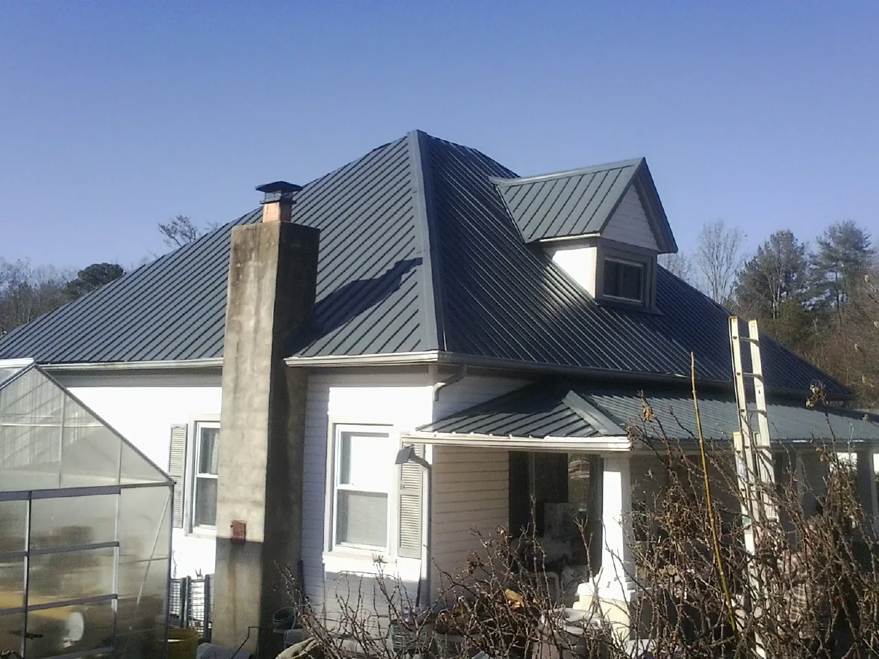 Dark blue standing seam metal roof on a white farmhouse with dormer — Slate & Tile Roof Repair by Roofing Brothers in Manzanola