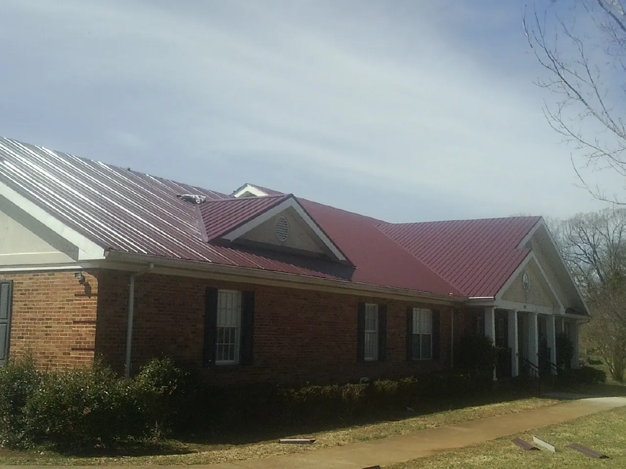 Red metal roof with gabled entries on a long brick building, from a Hail Damage Roof Repair job in Manzanola