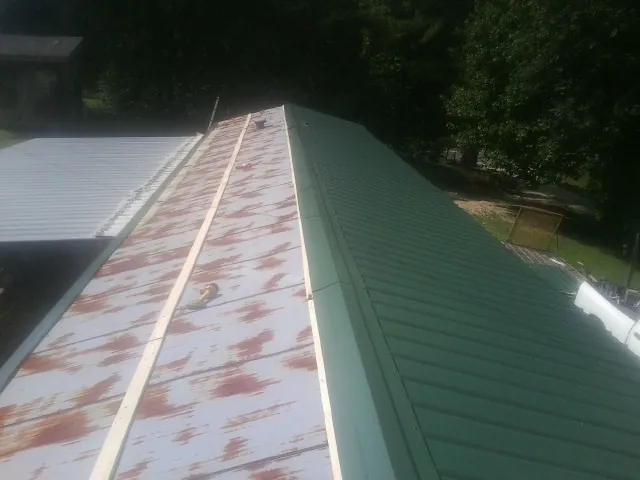 Old rusted panels beside newly installed green metal roofing — Wind Damage Roof Repair by Roofing Brothers in Manzanola