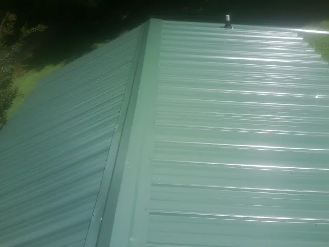 New green metal panels meeting at the ridge of a roof — Flat Roof Repair work by our crew in Manzanola