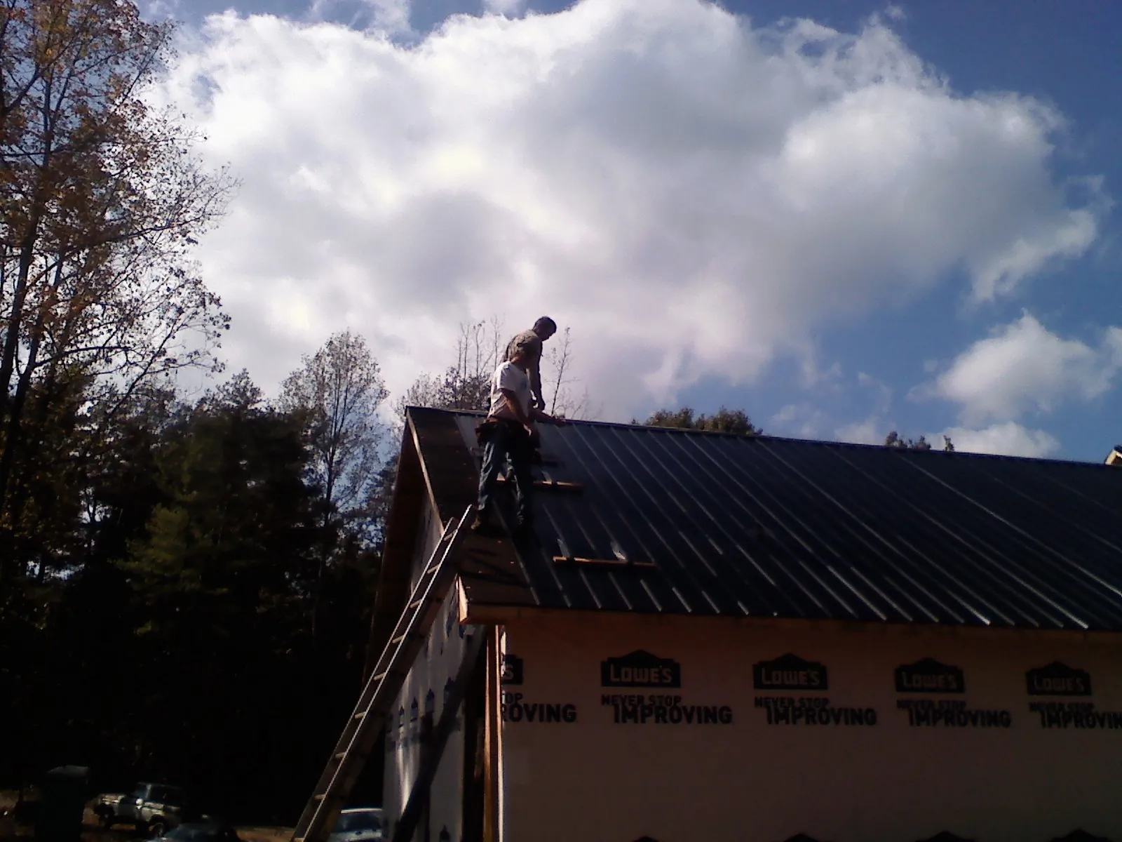 Roofer fastening dark metal panels high against a cloudy sky, from a Roof Inspection job in Manzanola