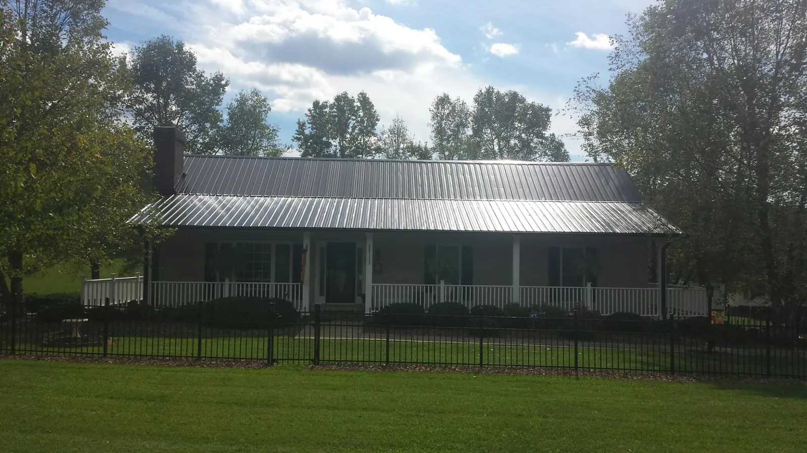 Gray metal roof on a brick ranch with a full width front porch — Gutter Guard Installation work by our crew in Manzanola