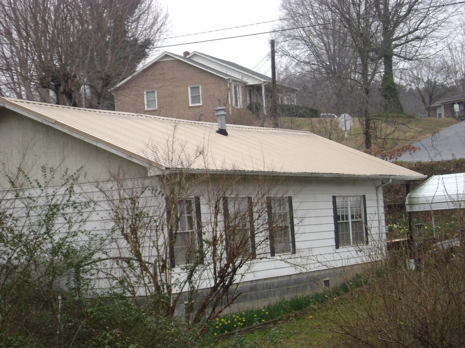 Tan metal roof on a white sided house set into a hillside — Commercial Roofing by Roofing Brothers in Manzanola