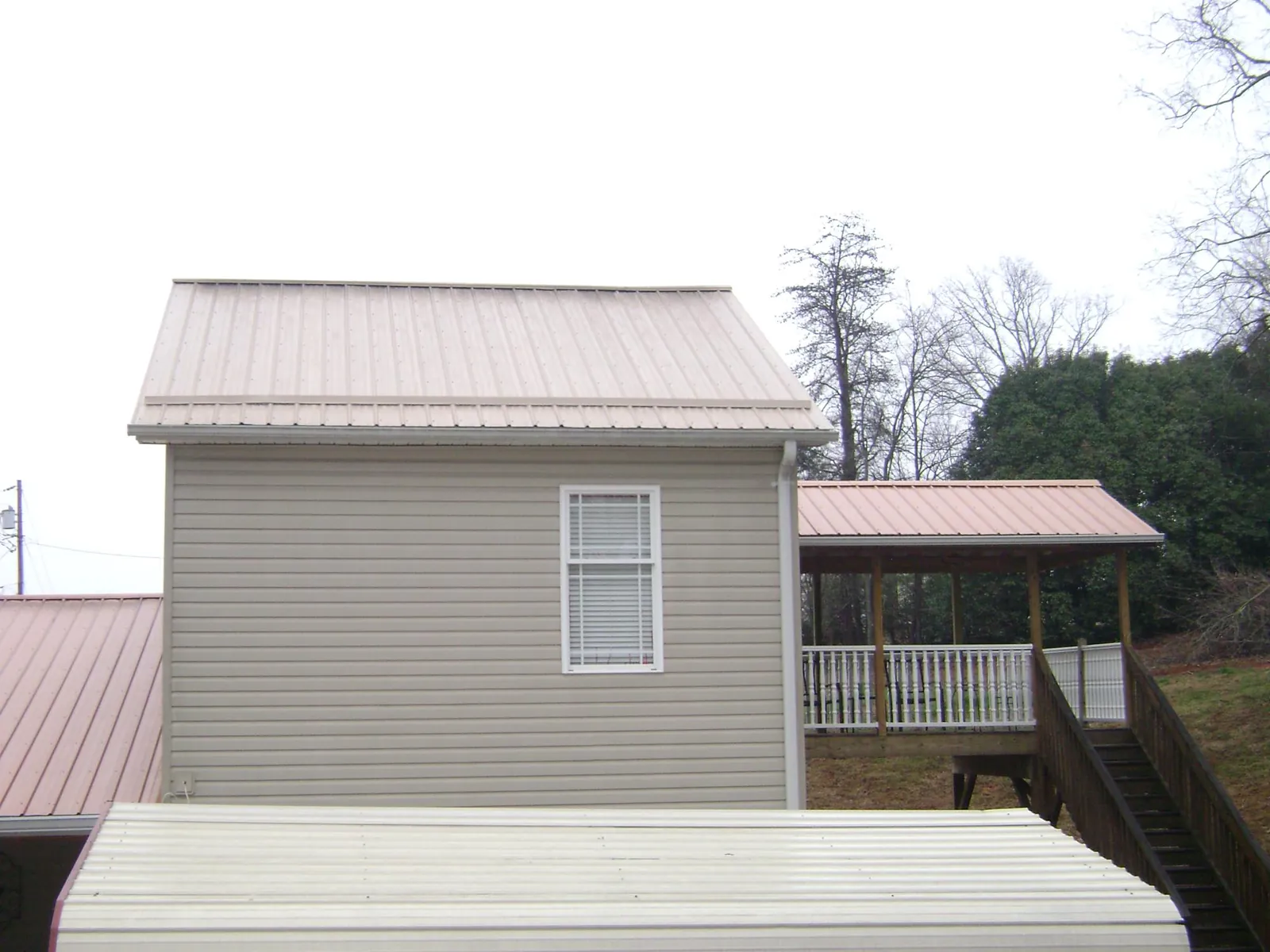 Tan metal roofs on a two story addition and attached porch, from a Roof Replacement job in Manzanola
